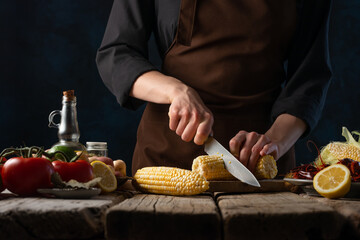 The cooking chef cuts the corn to make a dish with crayfish and potatoes. Recipe book and cooking