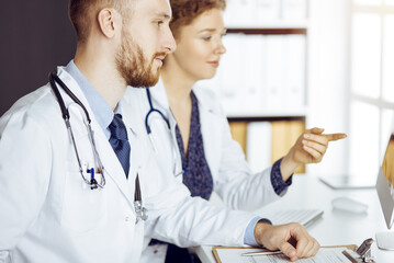 Bearded doctor with female colleague discussing current disease therapy while sitting at working...