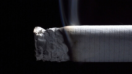 Photo of smoldering cigarette with filter on black