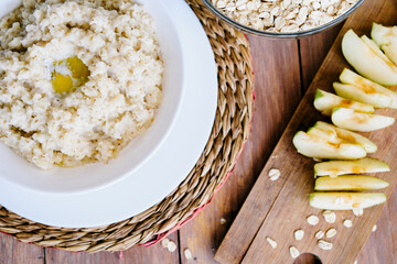 Porridge and apple with cinnamon. Oatmeal. Top view, space for text. Wooden background. A white plate.