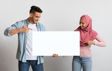Happy Millennial Islamic Couple Holding And Pointing At Long Blank Placard