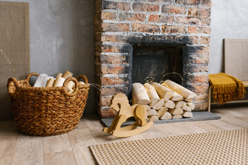 Red brick fireplace with firewood and a basket of firewood near it, children's wooden toy horse gurney in the living room in the Scandinavian style