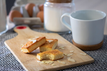 Gros plan sur un financier en partie mangé sur une planche à découper parsemé d’amandes effilées