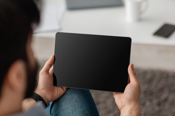 Unrecognizable guy using digital tablet with empty screen, browsing internet or showing new app, sitting on floor