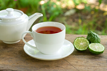 Bergamot tea or Earl Grey tea in white cup and fresh bergamot fruit with sliced on wooden table and blur background.