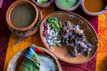 Mexican chopped lamb meat, hot sauces, and tortillas on colorful tablecloth