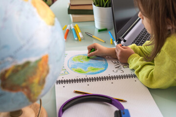 Wide angle view of child girl draws planet earth with wax colors on school notebook for Earth day -...