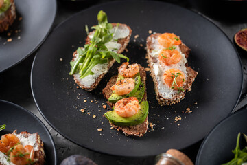 Three full grain sandwiches with cream cheese, avocado, shrimp and arugula on black plate