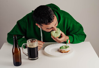 Un hombre soltero desayunando donuts con cerveza negra para celebrar el día de san patricio - obrazy, fototapety, plakaty