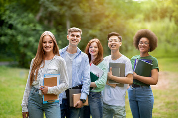 Group of interracial students with workbooks in hands posing outdoors in park