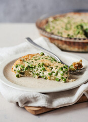 A slice of savoury pie with peas on beige plate on light-colored napkin and a whole shepherd's pie...