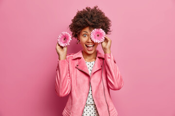 Positive female florist covers eyes with fragrant gerbera flowers makes bouquets for special...
