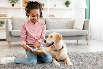 Young afro girl reading book with dog at home