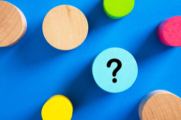Question mark icon on blue wooden block on blue background.