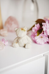 A grey concrete figurine of a teddy bear on a white surface surrounded by pink cherry blossom