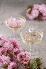 Two champagne glasses with splashes of champagne and pink cherry blossom on a grey surface