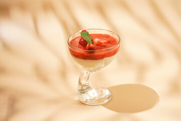 A glass of traditional italian creamy pudding dessert panna cotta with peppermint, strawberry jam, fresh strawberries with hard light shadow