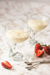 Two glasses with a traditional creamy pudding dessert panna cotta and surrounded fresh strawberries on a marble surface