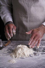 A male chef cook in a white shirt and grey apron making dough
