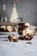 Almond half-chocolate biscuits sprinkled with chopped peanuts and placed on top of each other and milk bottle on light background