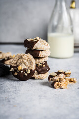 Almond half-chocolate biscuits sprinkled with chopped peanuts and placed on top of each other and milk bottle on light background