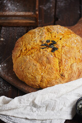 Loaf of whole orange pumpkin bread with pumpkin seeds on wooden board on wooden table
