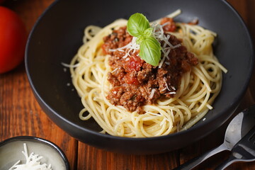 spaghetti with bolognese tomato sauce and fresh basil in black bowl on wooden table