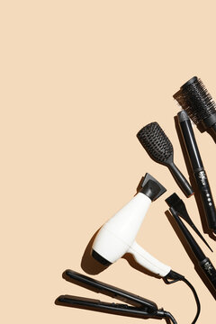 Hair brushes, hair dryer and curling wands: tools for hairdresser on pastel yellow background in hard light arranged as a side frame, a template, flat lay