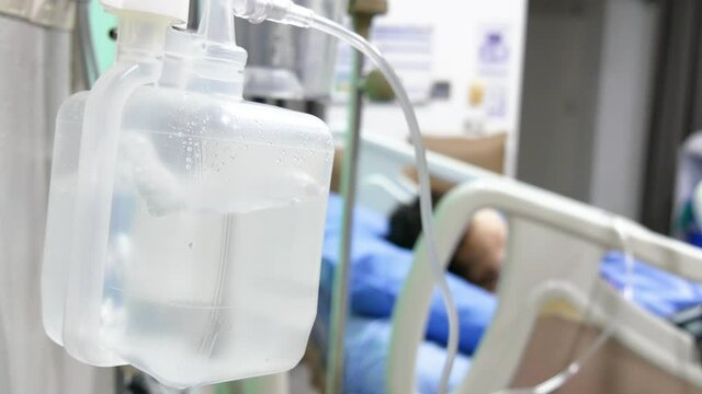 Oxygen humidifier for nasal cannula, patient on hospital bed on blurred background.