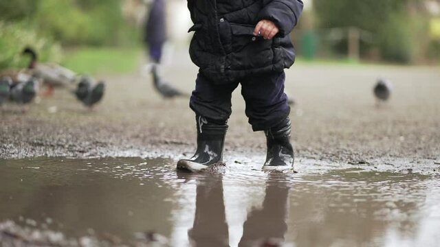Child running in water puddle wearing rain boots