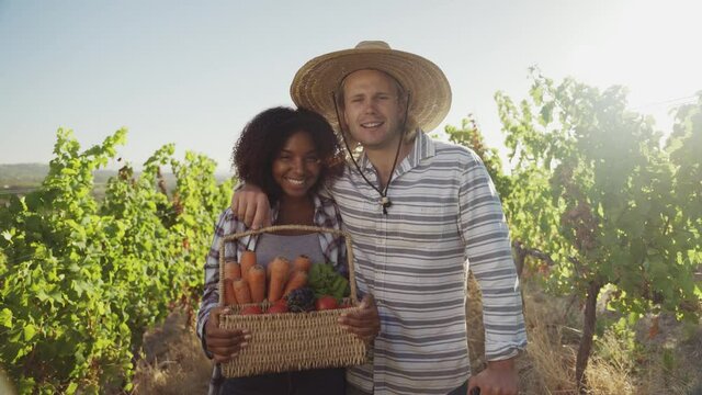 Mixed race male and female farmer colleagues standing smiling holding freshly picked vegetables 