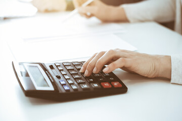 Accountant checking financial statement or counting by calculator income for tax form, hands closeup. Business woman sitting and working with colleague at the desk in office. Tax and Audit concept