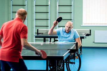 Adult disabled man in a wheelchair play at table tennis with his coach