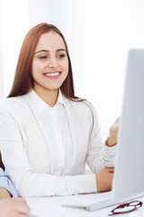 Young woman sitting at the desk with computer in sunny office. Looks like student girl or business lady communicating with casual dressed man
