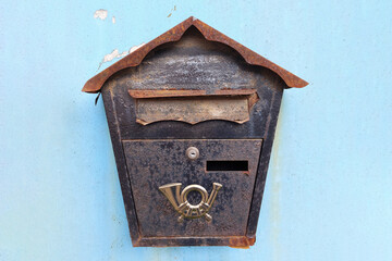 Old rusty mailbox on a blue metal fence.