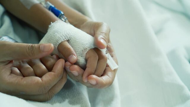 Young mother is holding hand bandaged of little daughter with comforting while they lying in the hospital bed sleeping. Recovering little girl. Hopeful emotional moment in ward. Focus on the hands.