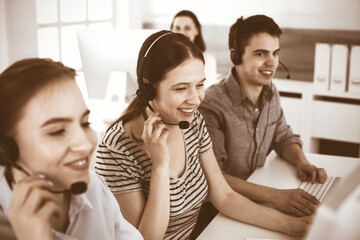 Casual dressed young woman using headset and computer while talking with customers online. Group of operators at work. Call center, business concept