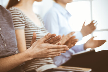 Obraz premium Business people clapping at meeting or conference, close-up of hands. Group of unknown businessmen and women in modern white office. Success teamwork, corporate coaching and applause concept