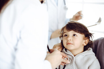 Woman-doctor examining a child patient by stethoscope. Cute arab toddler and his brother at physician appointment. Medicine concept