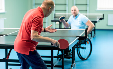 Adult disabled man in a wheelchair play at table tennis with his coach