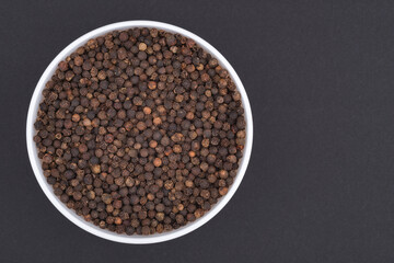 White glass bowl of black pepper. Isolated on a dark grey background. Top view close up