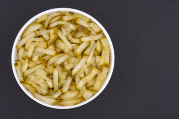 White glass bowl of sliced salted cucumber. Isolated on a dark grey background. Top view close up