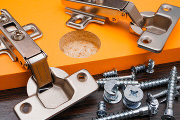 Various furniture fittings. Furniture assembly kit,  Concealed hinge and various screws on orange board.
