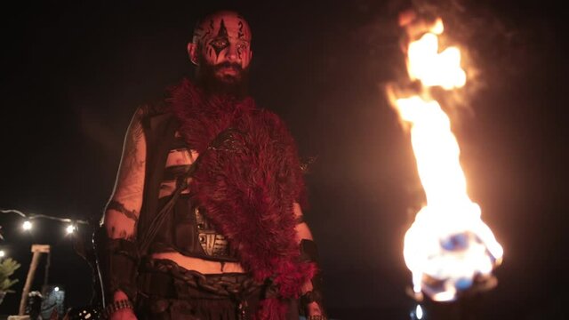 Viking with a torch lights bonfire. Brutal male warrior of dangerous appearance by the fire. The concept of ancient traditions wild life barbarian conquerors.