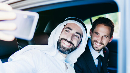The sheik and the businessman take a selfie in the car.