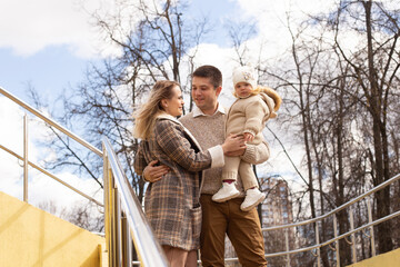 A young, beautiful couple is walking in the park with their little daughter.