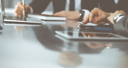 Unknown businessmen and woman sitting, using laptop computer and discussing questions at meeting in modern office, close-up