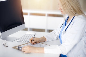 Unknown woman-doctor at work filling up medication history record form in sunny clinic, close-up