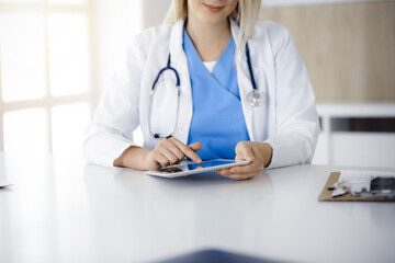 Unknown woman-doctor sitting in sunny clinic and using tablet pc, close-up. Data and best service in medicine