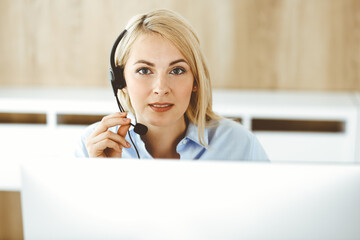 Blonde business woman sitting and communicated by headset in call center office. Concept of telesales business or home office occupation